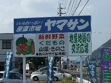 野菜や果物のイラストが描かれた産直市場ヤマサンの看板を映した写真
